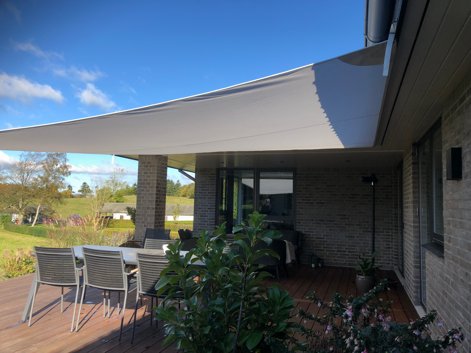 Stort solsejl over terrasse med spiseplads og udsigt over marker