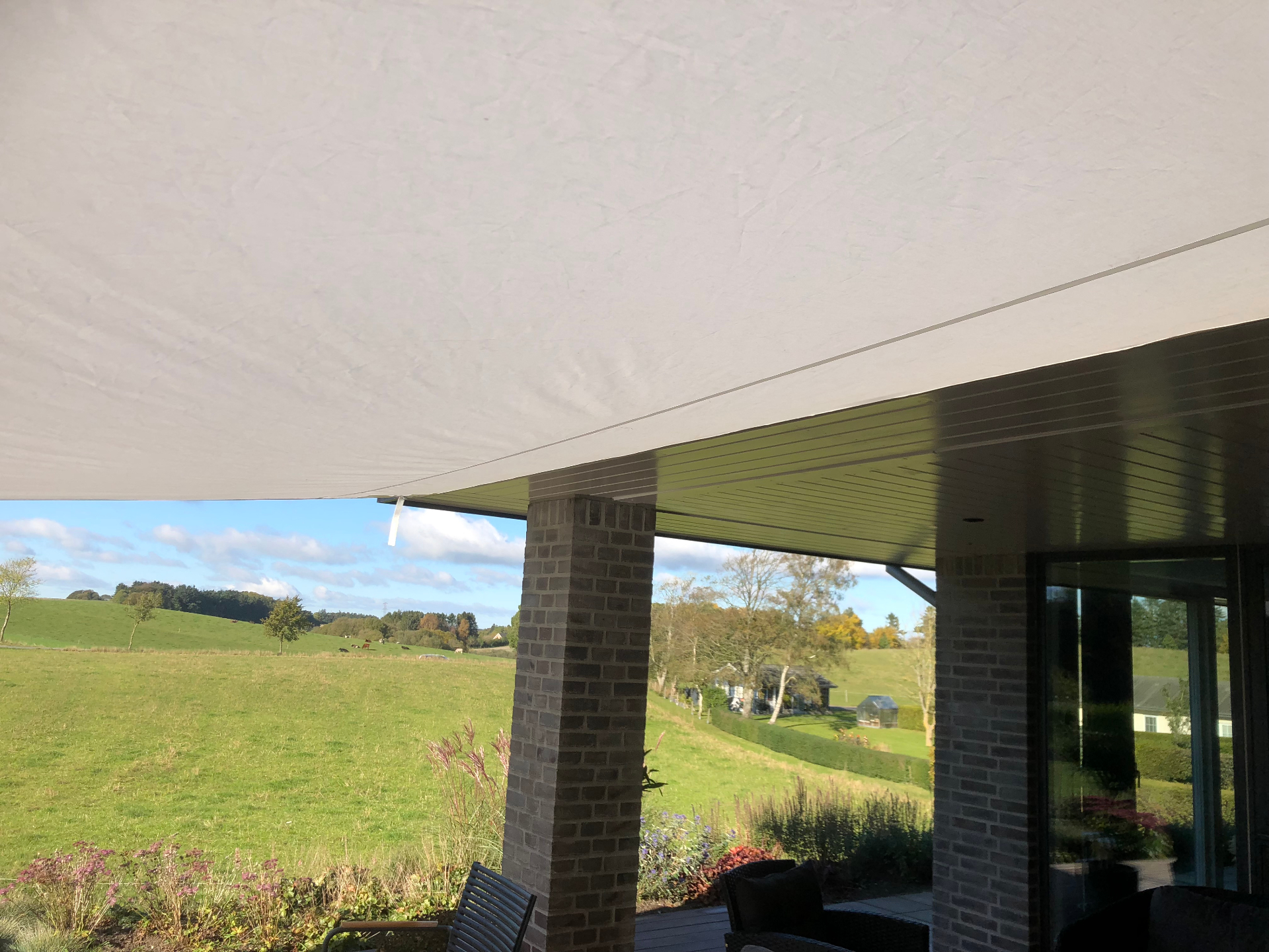 Solsejl set nedefra med udsigt over grønne marker og terrasse