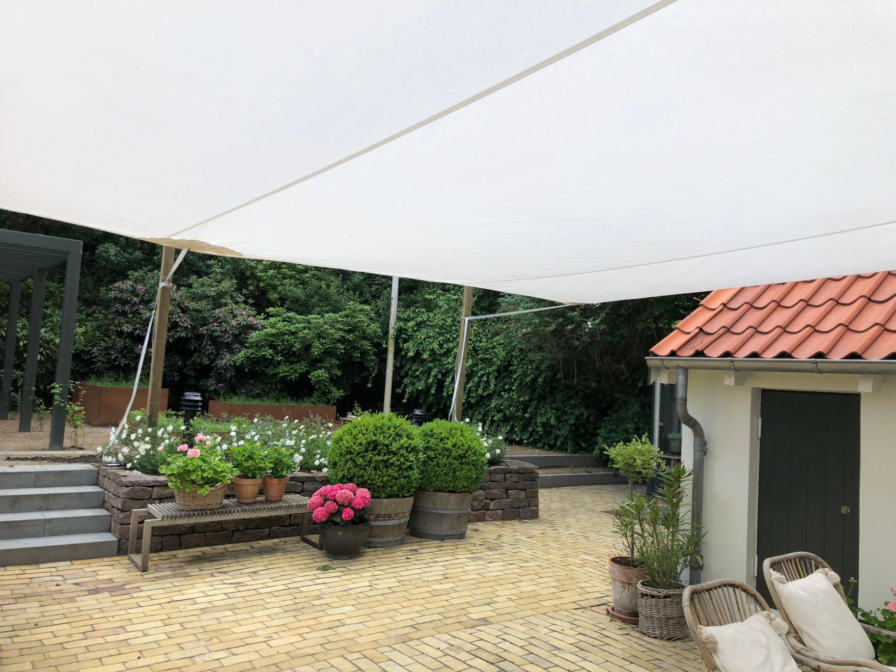 Stort hvidt solsejl over terrasse med blomster og krukker