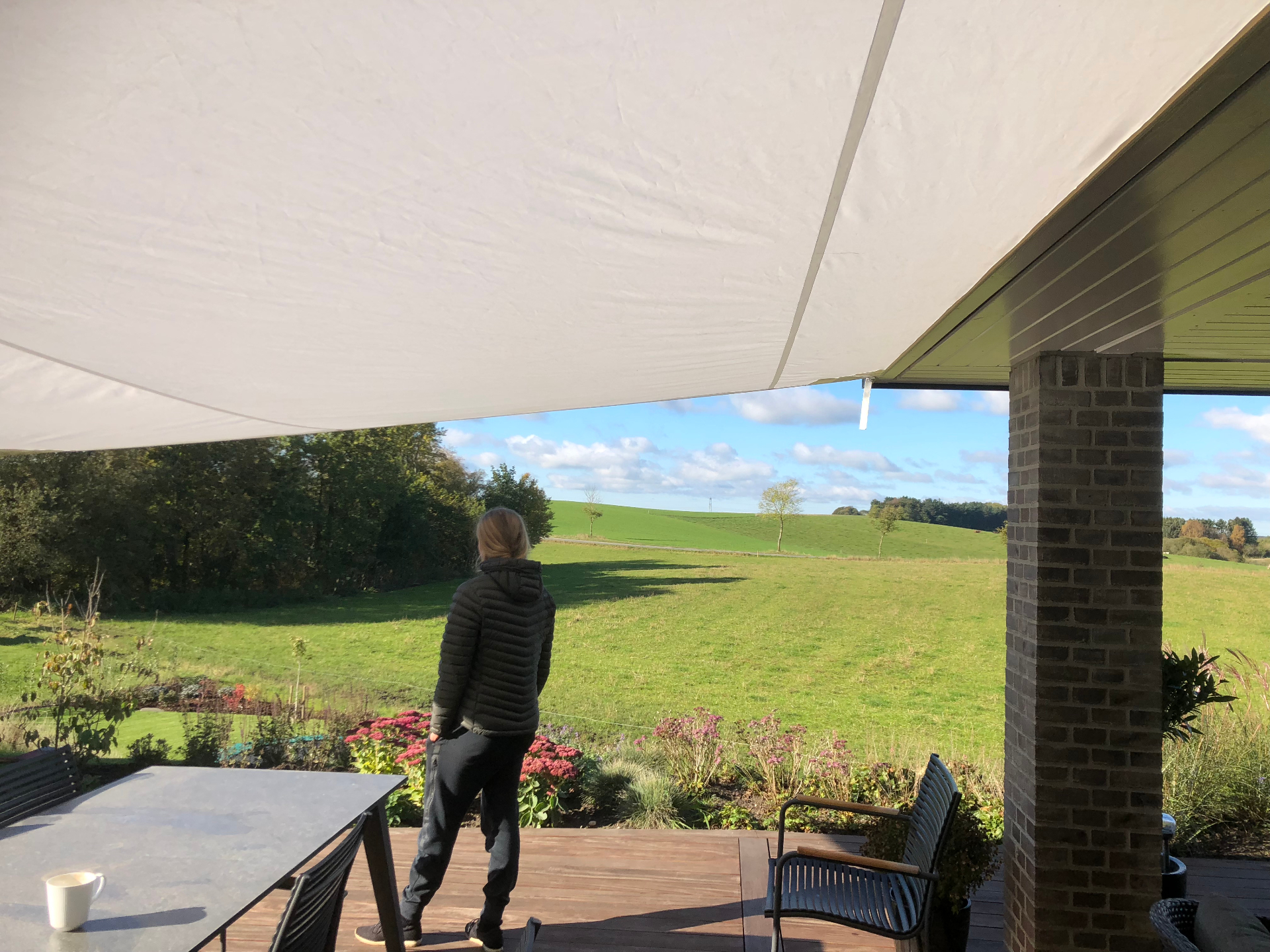 Solsejl over terrasse med panoramaudsigt over grønne bakker